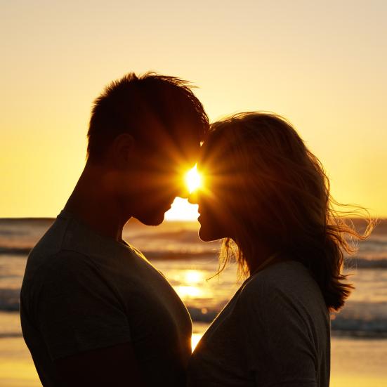 Ung mand og ung kvinde læner kærligt deres pander mod hinanden på en strand ved solnedgang.