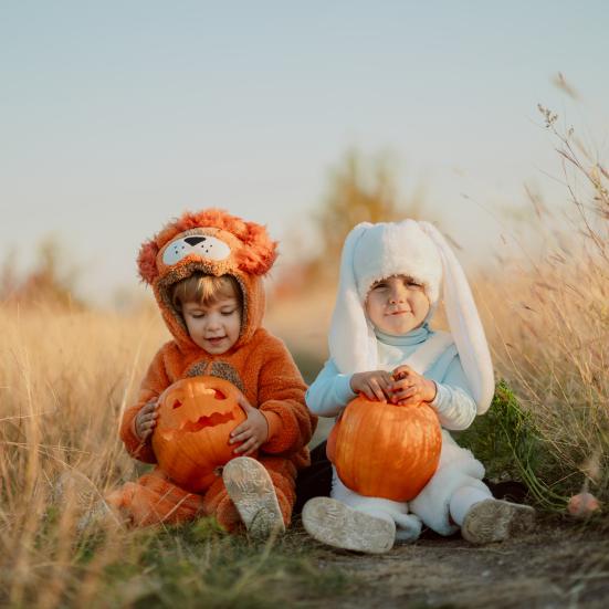 To søde børn sidder i græsset med halloweengræskar.