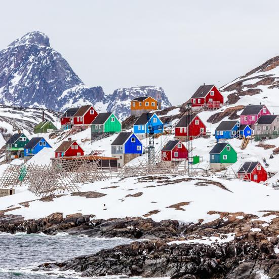 Farvestrålende grønlandske huse i landskab med sne og klipper.