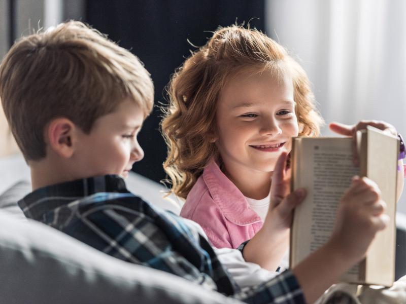 Glad dreng og pige læser i bog.