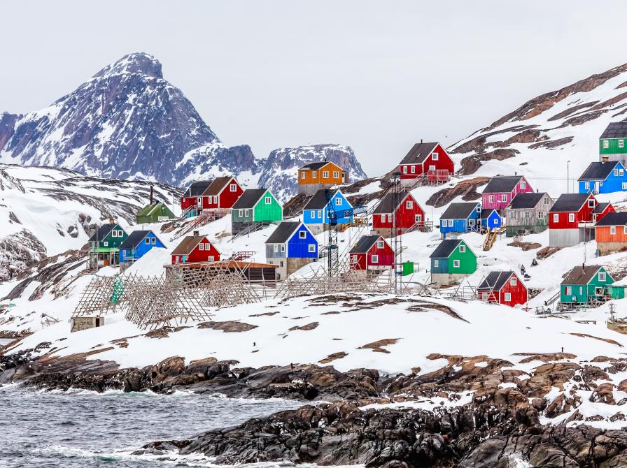 Farvestrålende grønlandske huse i landskab med sne og klipper.